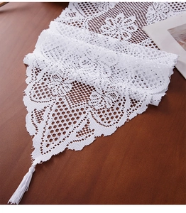 Detail of white crochet lace table runner with hollow floral patterns and long tassels