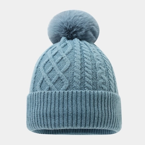 Detaillierte Zopfmuster-Textur und großer Kunstfell-Bommel an einer graublauen Wintermütze