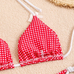 Detail of red and white gingham bikini top with delicate white bows on soft plush rug