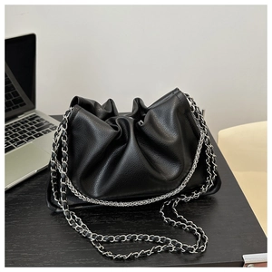 Detail of black pleated cloud bag with silver metal chain strap on a black desk