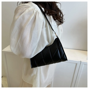 Detail of a black quilted shoulder bag with glossy finish and slim strap on minimalist background