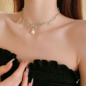 Détail du collier à nœud argenté avec strass et pendentif perle porté au cou
