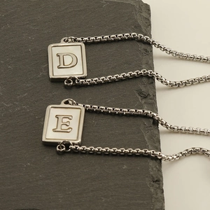 Macro detail of square white shell charms with silver letters D and E on sleek link chain