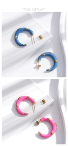 Flat display of C-shaped blue and pink enamel earrings with golden accents on white background