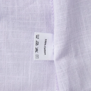 Makroaufnahme der lavendelfarbenen Baumwollkleid-Textur und des 100% Baumwolle-Etiketts