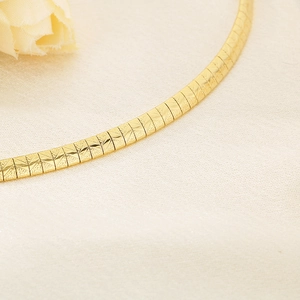 Detailed view of the flat golden textured snake chain necklace on a soft fabric background