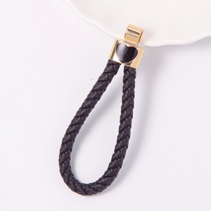 Macro detail of black braided leather keychain with gold heart charm on white background
