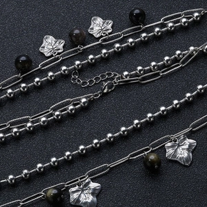 Macro detail of double-layered stainless steel necklace with black beads and leaf pendant