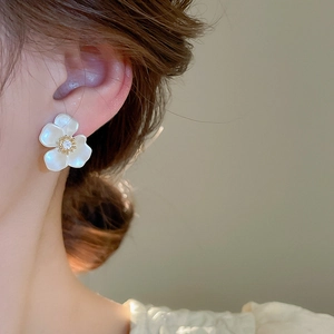 Detailed close-up of a zircon flower earring with white petals and golden core on ear
