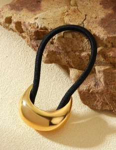 Detail of a crescent-shaped gold metal hair clip with a black elastic hair tie on a rock