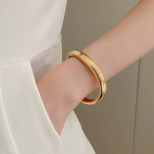 Close-up of minimalist polished gold bangle bracelet showing glossy metallic mirror finish