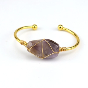Macro detail of handmade gold wire-wrapped purple raw crystal on an open bangle bracelet