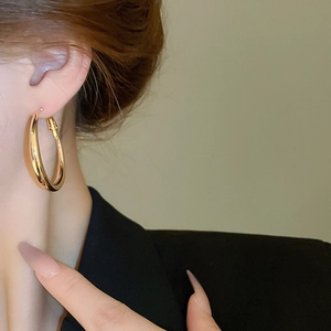 Close-up of large gold hoop earrings with a polished mirror finish on model's ear