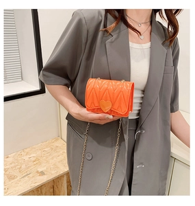 Close-up of bright orange heart-shaped buckle and quilted texture on mini chain bag