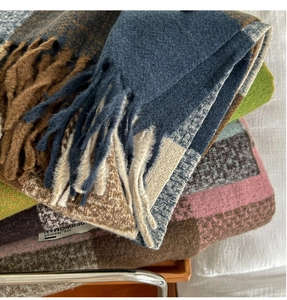 Close-up of stacked plaid scarfs showing thick wool texture and soft fringe details