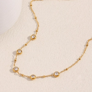 Détail d'un collier plaqué or 18 carats avec zircons ronds et perles sur fond beige