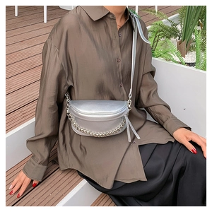 Silver crescent saddle bag with metallic chain detail worn by model in outdoor setting