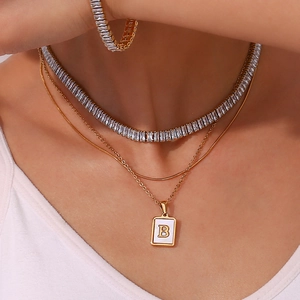 Close-up of layered gold necklaces with zircon tennis chain and letter B pendant
