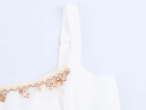 Detail shot of white beach dress featuring shell and starfish charms on woven straps
