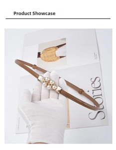 Detail of slim brown leather belt with pearl and rhinestone gold buckle held by a hand