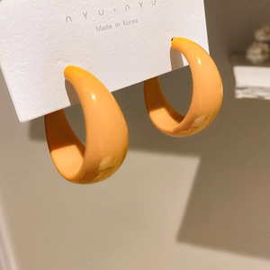 Detailed close-up of wide C-shaped orange hoop earrings with glossy resin texture