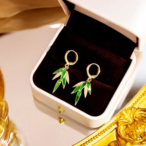 Detail of gold bamboo leaf earrings with green enamel and white crystals in a jewelry box