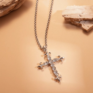 Detailed view of silver cross pendant with fleur-de-lis and rhinestones on stone background