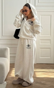 Détail de l'ensemble sweat à capuche brodé gris et pantalon large dans un décor d'intérieur