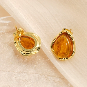 Detail of amber resin water drop earrings with golden metal borders on silk fabric