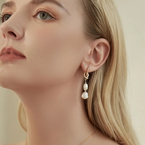 Minimalist baroque pearl drop earrings with golden knot design worn by a model