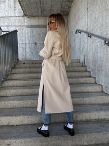 Detail view of the side slit and waist tie on this long beige wool coat for women