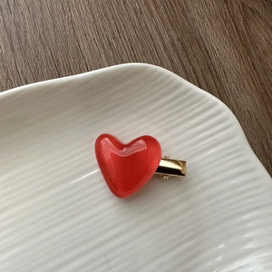 Detail of a shiny red heart jelly hair clip on a white ceramic plate and wooden background