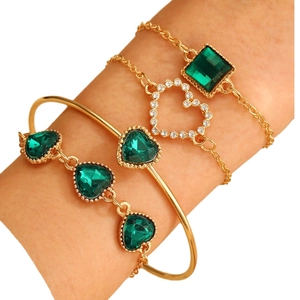 Four-piece gold bracelet set with green gemstones and heart charms on female wrist