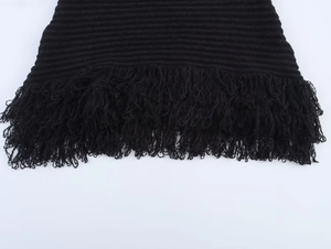 Dettaglio macro della trama in maglia nera e delle frange sull'orlo della gonna