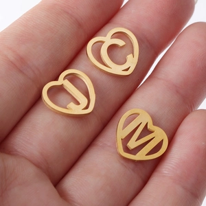 Golden hollow heart-shaped alphabet pendants C, J, M shown in palm for size scale