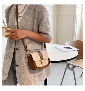 Detail of woven straw crossbody bag with brown leather trim and golden metal clasp
