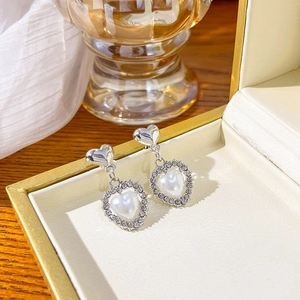 Detail of silver heart-shaped pearl earrings with rhinestones in a luxury jewelry box