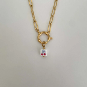 Detail of gold chain necklace with a square white pendant featuring red cherry pattern