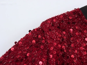 Dettaglio macro del tessuto con paillettes rosse e bordo nero su una giacca di tweed