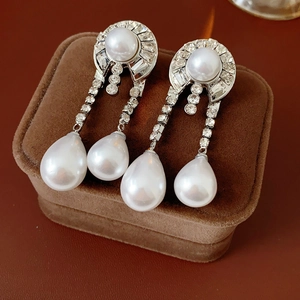 Detailed view of silver needle pearl tassel earrings with rhinestones on brown velvet box