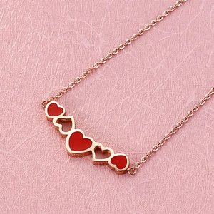 Close-up of rose gold necklace featuring red enamel hearts on a textured pink surface