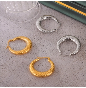 Detailed close-up of gold and silver twisted textured hoop earrings on a grey surface