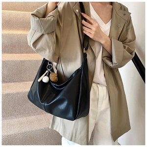 Detail of black hobo bag with baseball glove pendant on a khaki trench coat