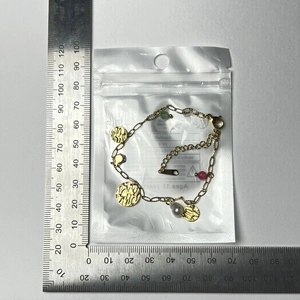 Détail d'un bracelet doré avec perles et breloques martelées à côté d'une règle