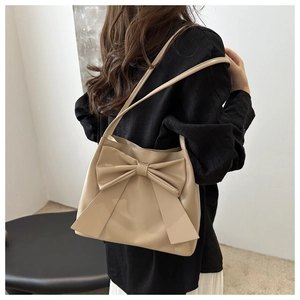 Detail view of large bow on apricot leather tote bag shown on model's shoulder