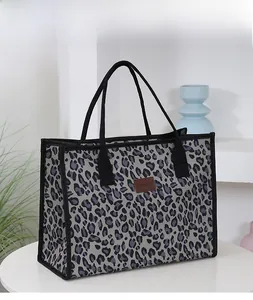 Close-up of leopard print canvas tote bag with black piping and brown leather logo patch