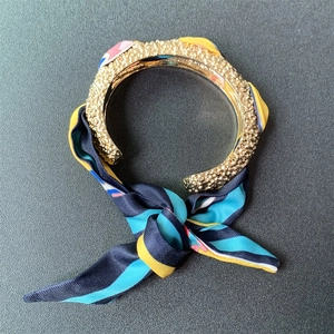 Close-up of matte gold textured open cuff bracelet with wrapped colorful silk scarf detail