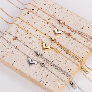 Three geometric heart necklaces in gold, rose gold, and silver on a textured stone