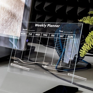 Detailed view of clear acrylic weekly planner board on office desk with metal stands