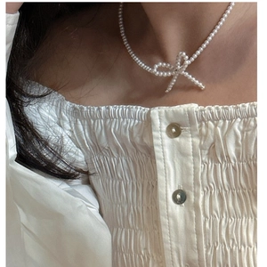 Detail of a white pearl bow necklace worn on neck with white elegant shirt background